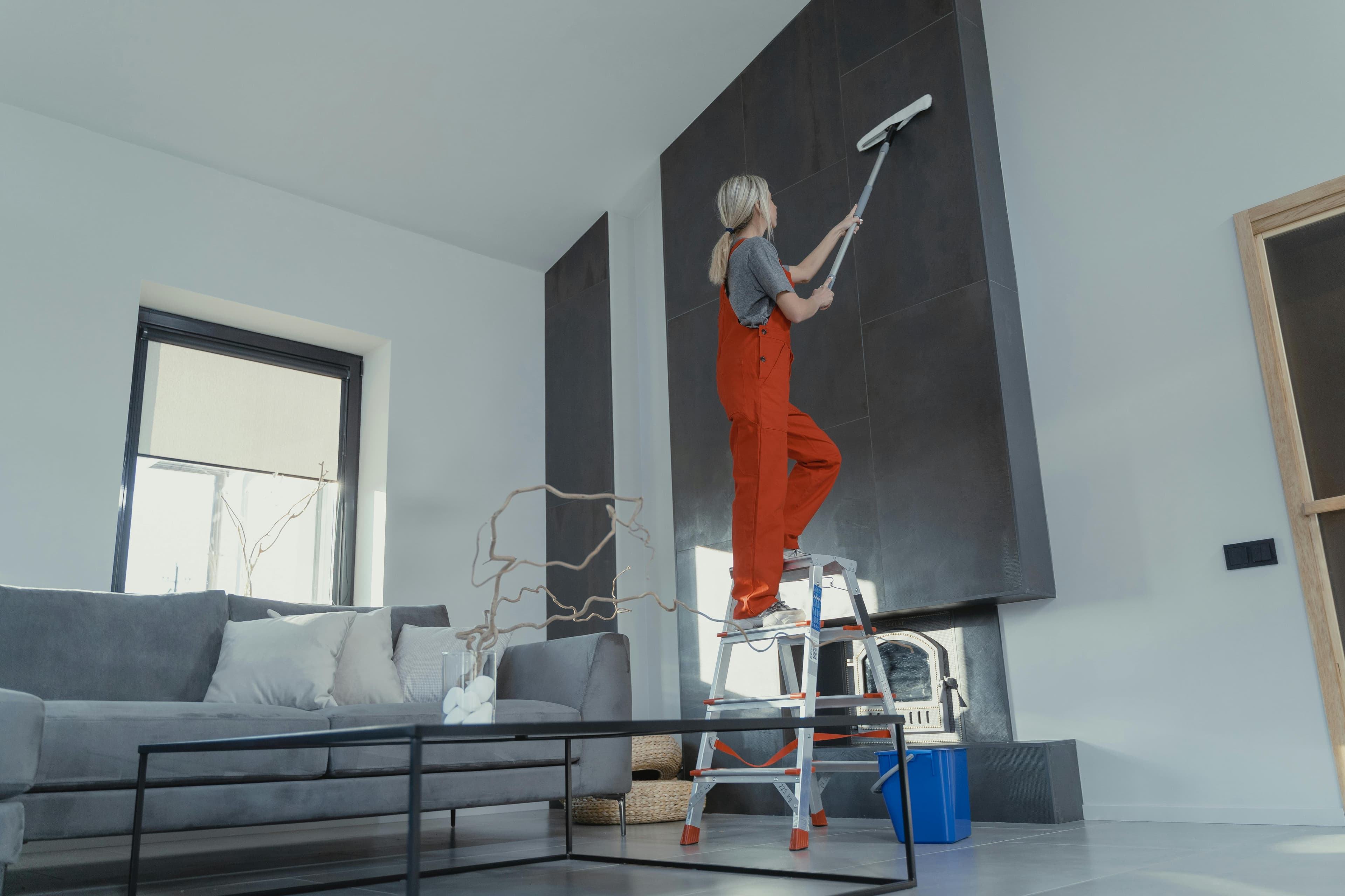 OCS technician on a ladder cleaning a tall surface after construction
